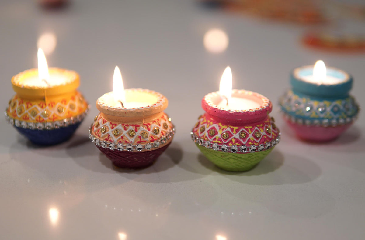 Two colorful clay pot wax diyas lit on a tabletop