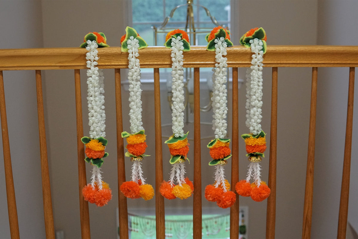 Five white artificial jasmine strings with orange and yellow floral accents displayed on a railing